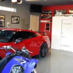 White tornado shelter in a garage next to a red car