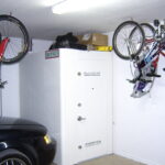 White storm shelter in a garage next to a black car and hanging bikes