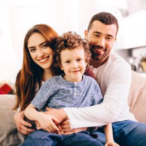Family of three smiling and sitting on the couch