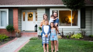 a smiling family standing outside their home