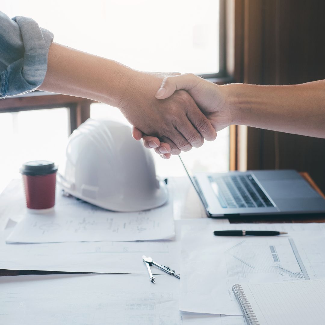 Shaking hands over a table with a hard hat and blue prints