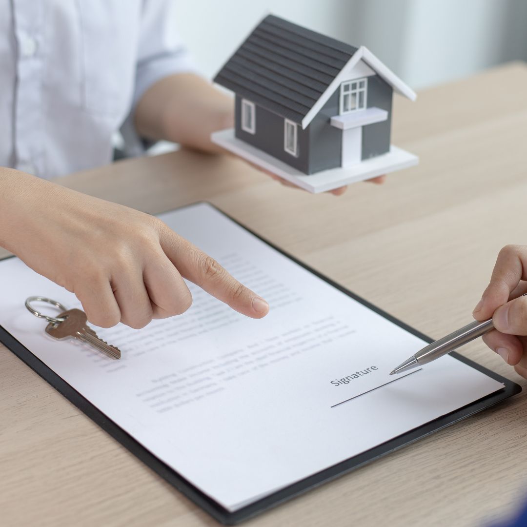 Person signing a contract with house model and keys