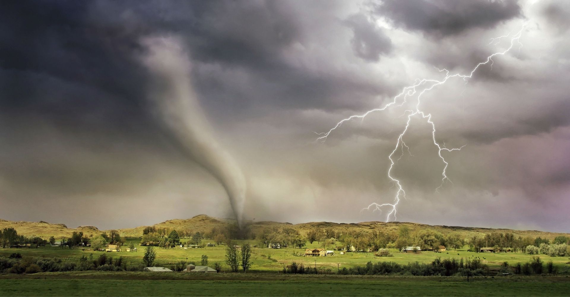Tornado and lightning over rural landscape with dark clouds