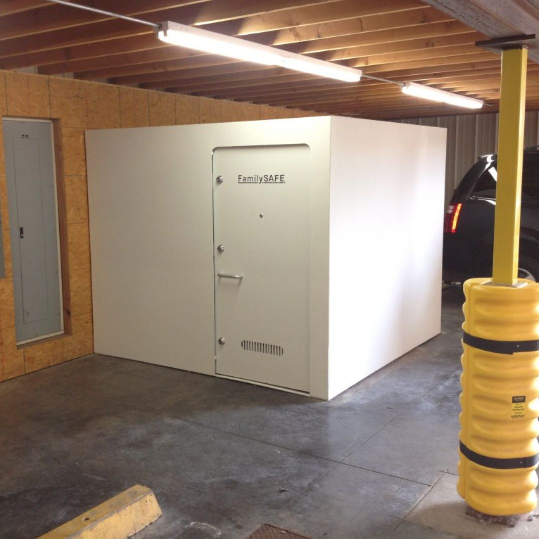 Indoor garage with white storm shelter beside a car